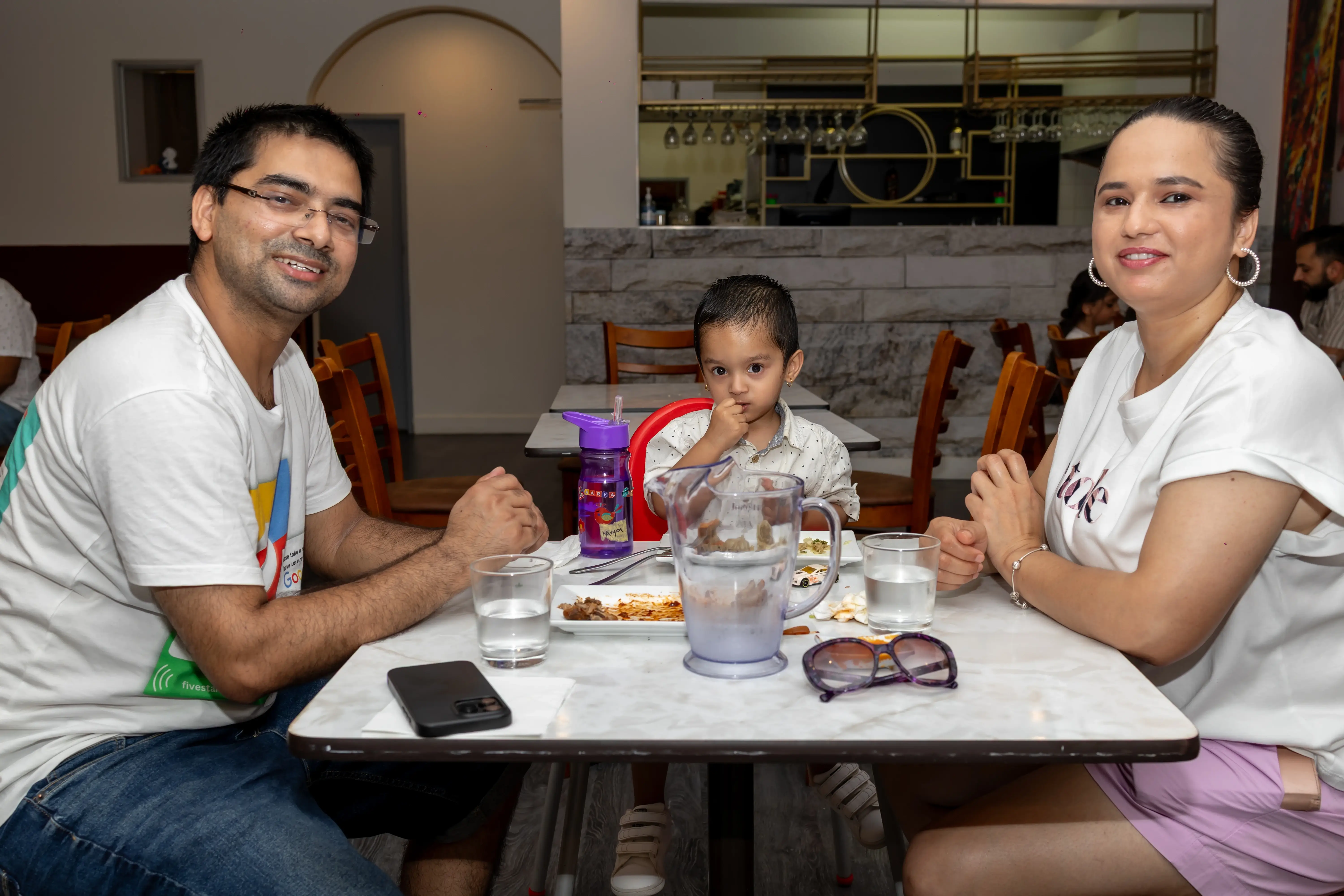 A couple and their young baby enjoying food while seated in semi-formal attire. They are smiling at the camera and having fun, with the table featuring kid-friendly food while the couple enjoys their meal at Third Eye Windsor, 515 George St, South Windsor NSW 2756.